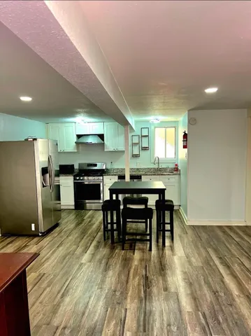 a kitchen with stainless steel appliances kitchen island granite countertop a refrigerator a stove a sink a dining table and chairs with wooden floor