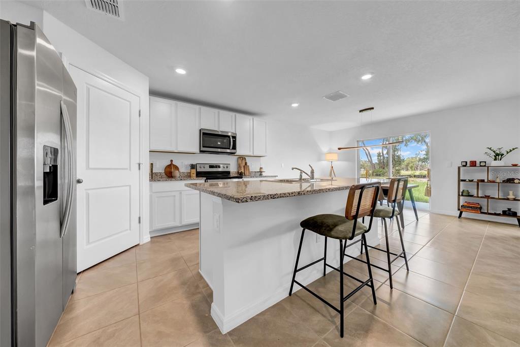 13295 Mylion Way Spring Hill, FL 34610 - Photo 5 of 68 a kitchen with stainless steel appliances kitchen island granite countertop a refrigerator a stove a sink a dining table and chairs with wooden floor