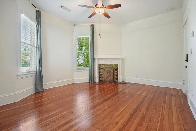 an empty room with wooden floor a chandelier fan and windows