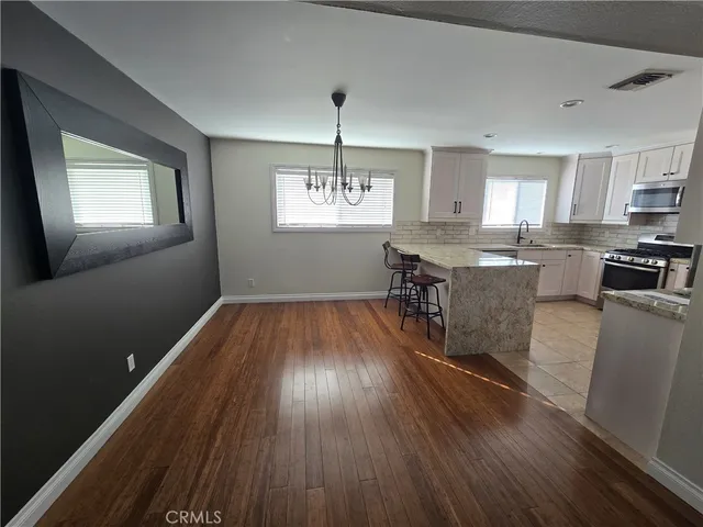 a kitchen with stainless steel appliances granite countertop a stove top oven a sink dishwasher and a dining table with wooden floor