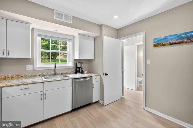 a kitchen with stainless steel appliances granite countertop white cabinets a sink a stove a refrigerator and microwave with wooden floor