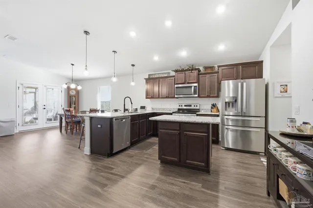 a kitchen with stainless steel appliances kitchen island granite countertop a large refrigerator a sink a stove and a wooden floors