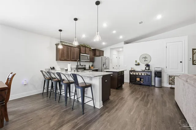 a kitchen with stainless steel appliances granite countertop a stove top oven a refrigerator a dining table and chairs with wooden floor