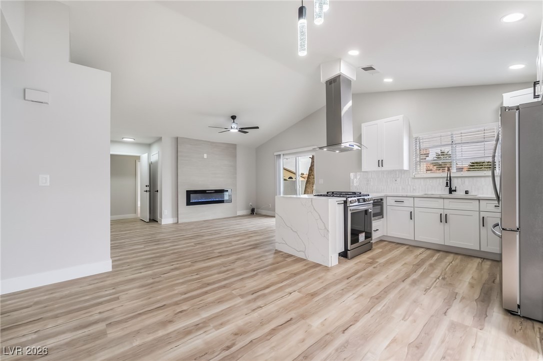 2850 Nikki Place Henderson, NV 89074 - Photo 64 of 64 Kitchen featuring open floor plan, stainless steel appliances, white cabinets, a fireplace, and light wood-type flooring