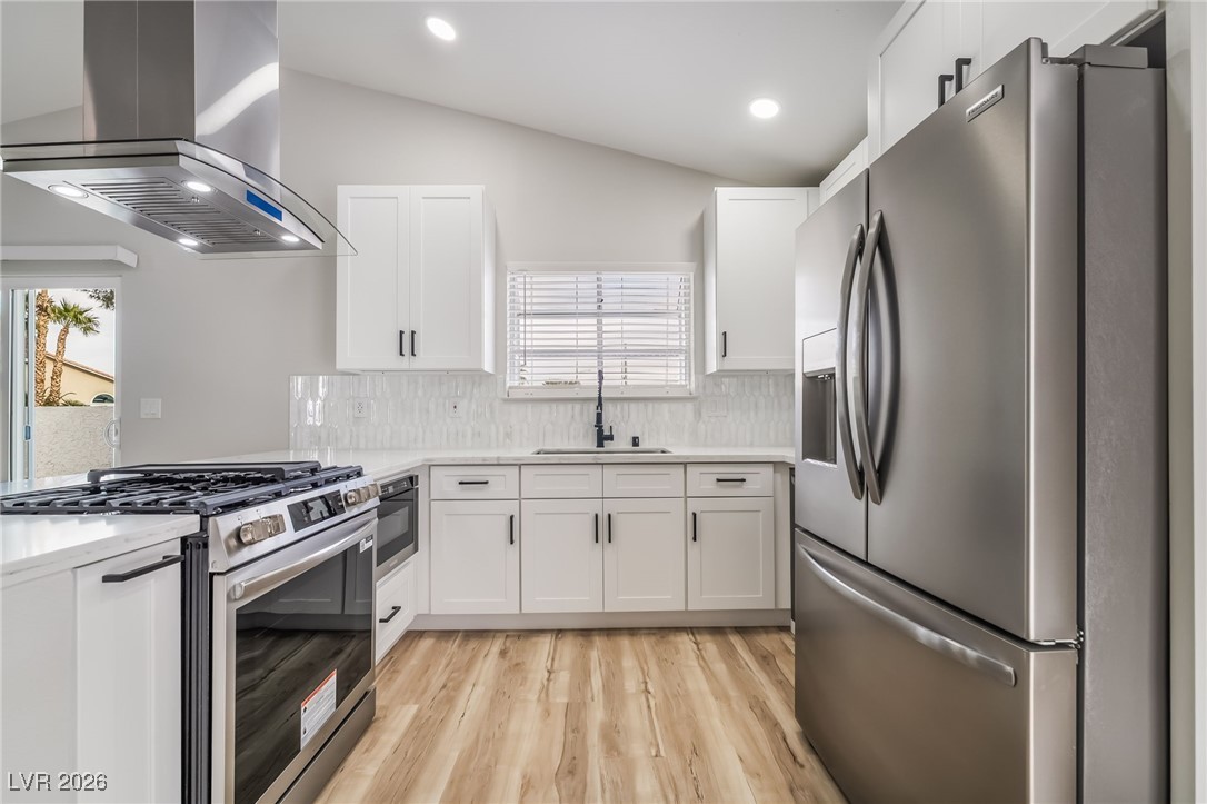 2850 Nikki Place Henderson, NV 89074 - Photo 12 of 64 Kitchen featuring appliances with stainless steel finishes, range hood, decorative backsplash, white cabinets, and vaulted ceiling