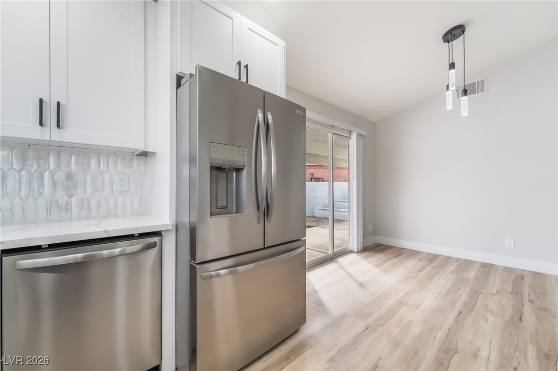 2850 Nikki Place Henderson, NV 89074 - Photo 15 of 64 Kitchen with stainless steel appliances, hanging light fixtures, light wood-style floors, white cabinets, and light stone countertops