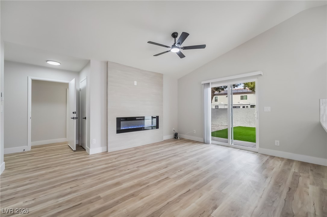 2850 Nikki Place Henderson, NV 89074 - Photo 7 of 64 Unfurnished living room with vaulted ceiling, light wood-style flooring, a large fireplace, and a ceiling fan