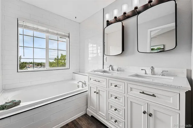 a bathroom with a granite countertop sink a large mirror a vanity and a bathtub
