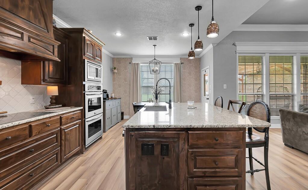 550 Hunton Lane Robinson, TX 76706 - Photo 11 of 35 Kitchen with a breakfast bar, light wood-style floors, backsplash, custom range hood, and an island with sink