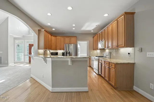 a kitchen with stainless steel appliances granite countertop a refrigerator a sink dishwasher a stove and a microwave oven with wooden floor