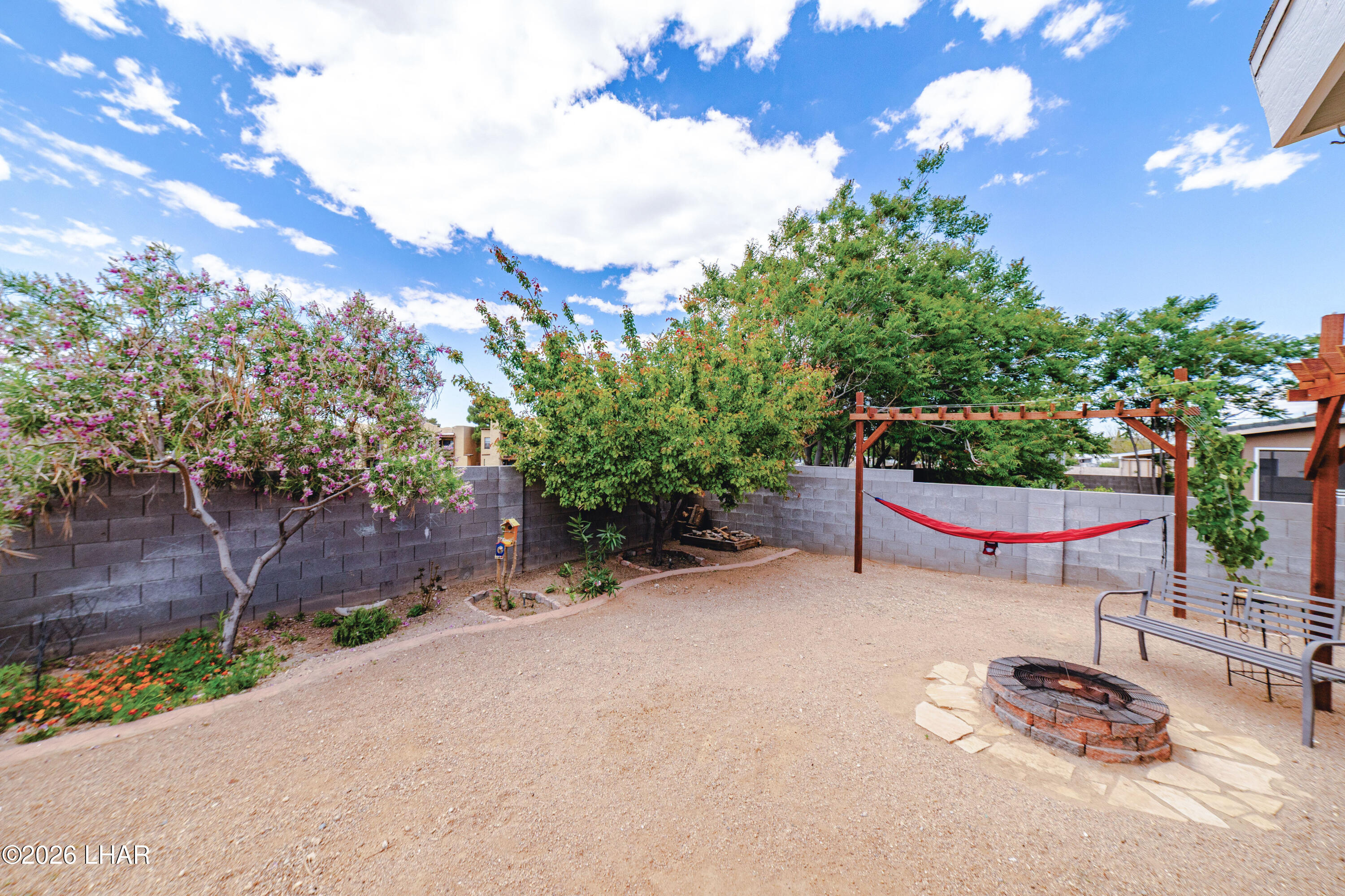 2177 Ridgeview Road Kingman, AZ 86401 - Photo 22 of 43 Backyard featuring a central fire pit with stone surround, a gravel-covered surface, and mature perimeter fruit and desert trees