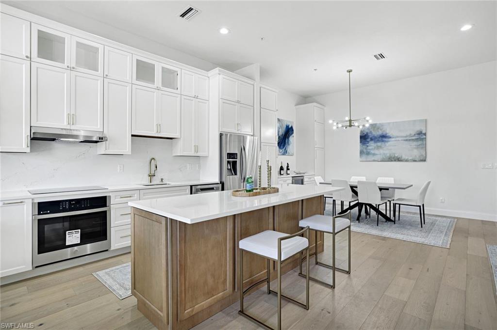 630 Lalique Circle, Unit 506 Naples, FL 34119 - Photo 8 of 25 a kitchen with stainless steel appliances granite countertop a stove top oven a sink dishwasher a dining table and chairs with wooden floor