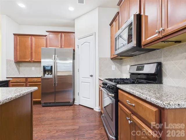a kitchen with stainless steel appliances granite countertop a refrigerator a stove and a sink with wooden floor