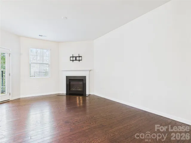an empty room with wooden floor fireplace and windows