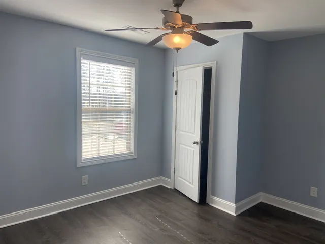 an empty room with wooden floor ceiling fan and windows