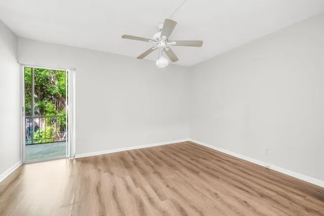 an empty room with wooden floor ceiling fan and windows