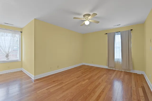 an empty room with wooden floor fan and windows