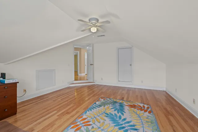 a view of an empty room with wooden floor and fan