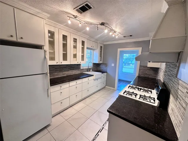 a kitchen with granite countertop a refrigerator stove and white cabinets