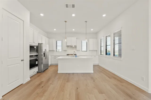 a large white kitchen with kitchen island a sink wooden floor and stainless steel appliances