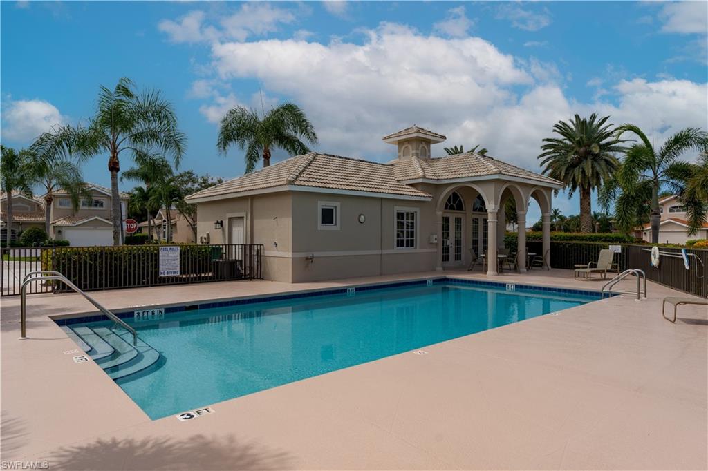 6658 Castlelawn Place, Unit 9 Naples, FL 34113 - Photo 37 of 38 Resort-style pool area featuring a large rectangular pool with integrated steps, a surrounding paved deck, and a clubhouse with a covered patio supported by archways