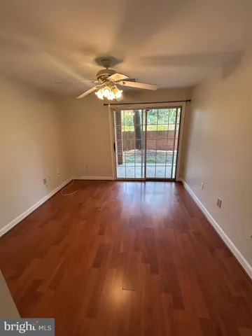 a view of an empty room with wooden floor and fan