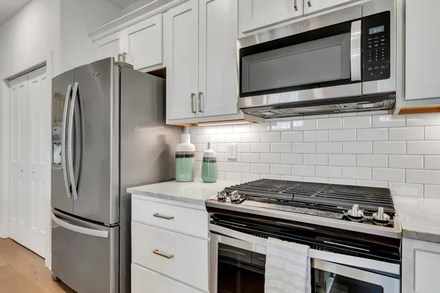 a kitchen with stainless steel appliances a stove top oven a sink a microwave a refrigerator and white cabinets