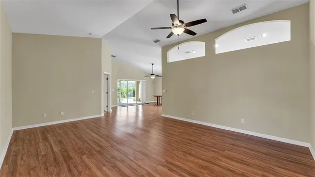a view of an empty room with wooden floor and a ceiling fan
