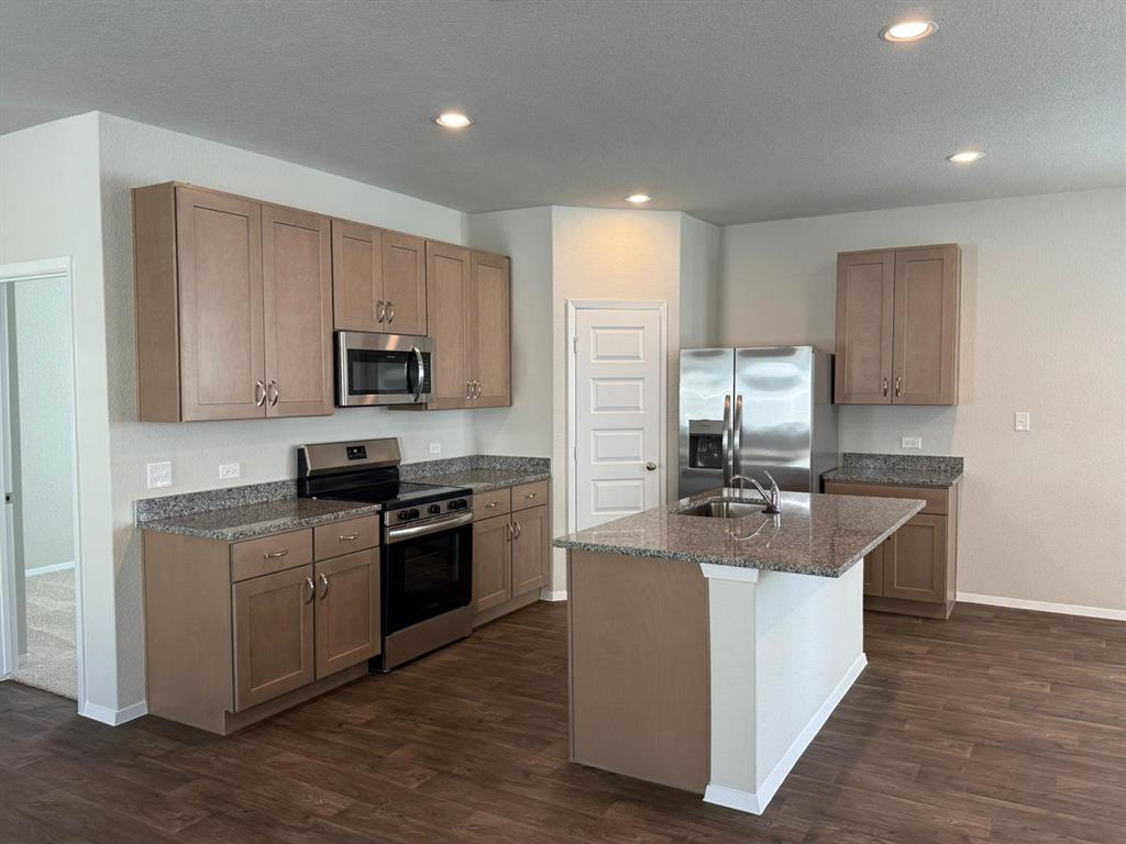 2707 Totley Road Manor, TX 78653 - Photo 8 of 39 Kitchen with stainless steel appliances, dark stone countertops, dark wood-type flooring, a kitchen island with sink, and recessed lighting
