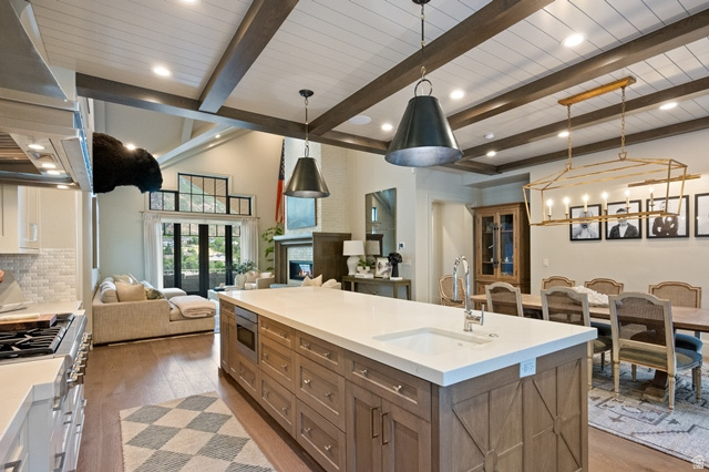 3 Carriagewood Cove, Unit 1088 Sandy, UT 84092 - Photo 20 of 79 Open-concept living space featuring a spacious kitchen island with integrated sink, wood-finish flooring, exposed ceiling beams, and a fireplace in the living area