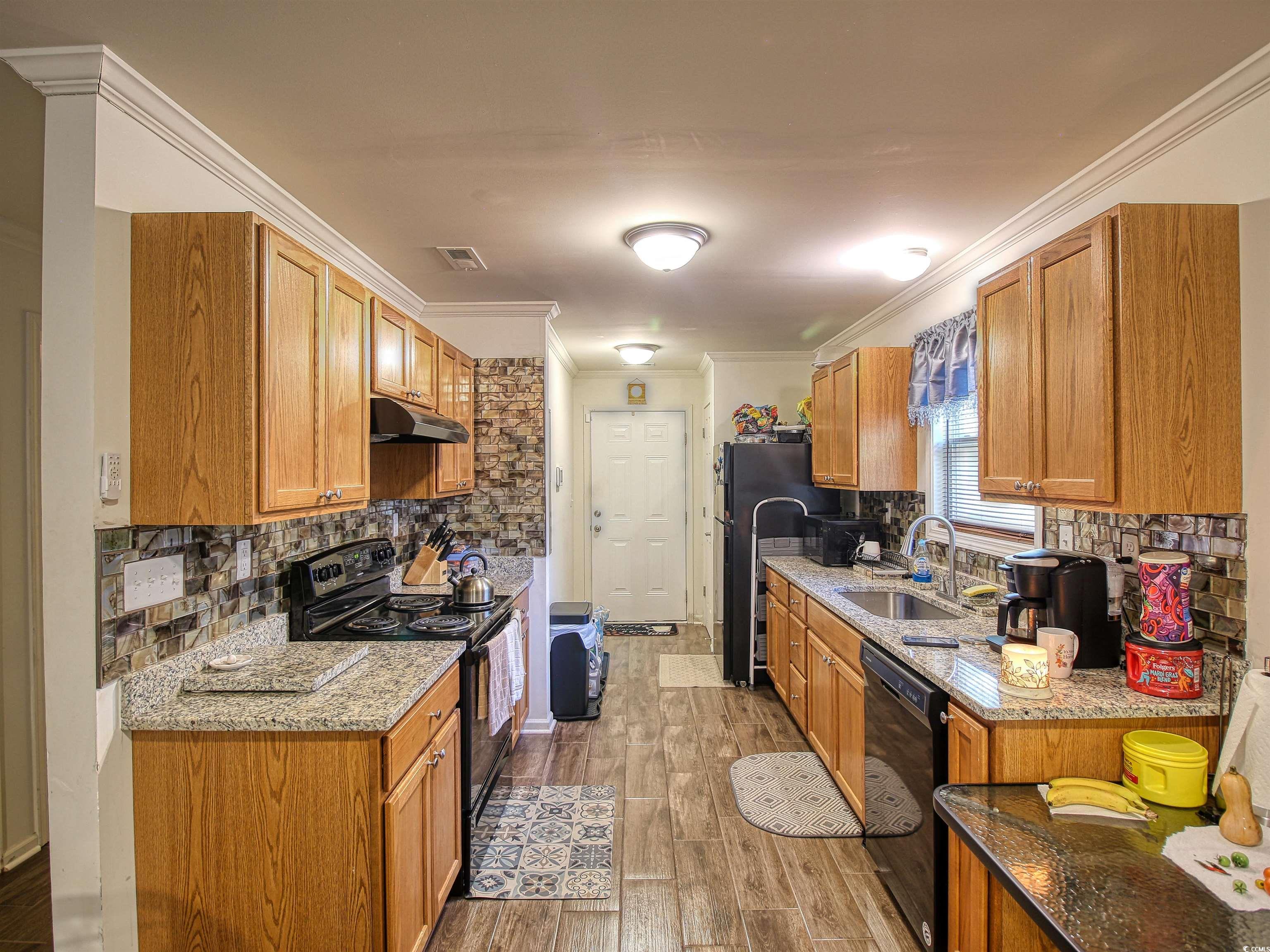 215 West James Street Mullins, SC 29574 - Photo 7 of 18 Kitchen featuring backsplash, black appliances, light stone countertops, brown cabinetry, and crown molding