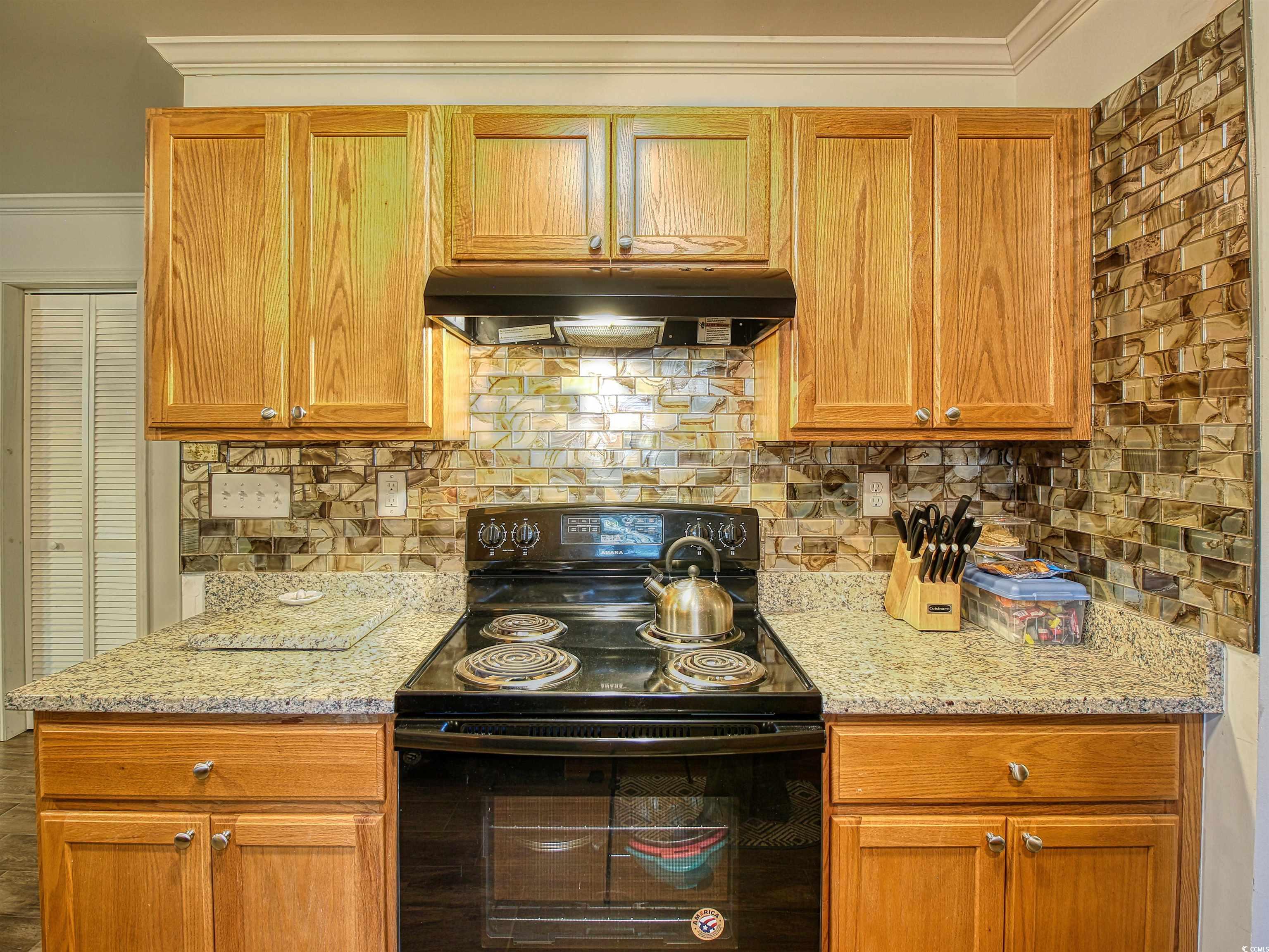 215 West James Street Mullins, SC 29574 - Photo 8 of 18 Kitchen with electric range, backsplash, light stone countertops, brown cabinetry, and crown molding