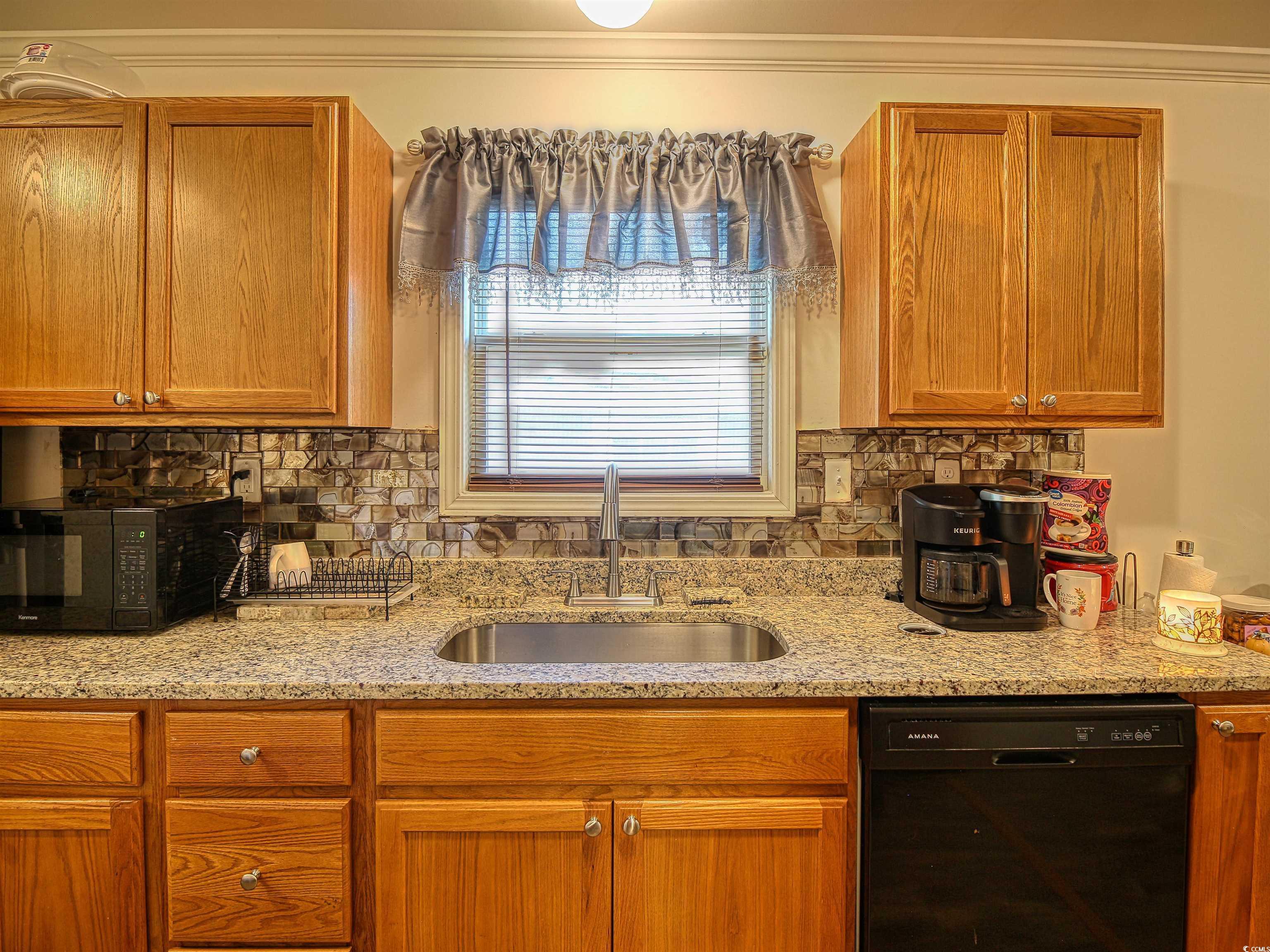 215 West James Street Mullins, SC 29574 - Photo 9 of 18 Kitchen with black appliances, brown cabinetry, backsplash, light stone counters, and crown molding