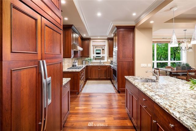 a kitchen with stainless steel appliances granite countertop a refrigerator a sink dishwasher and wooden cabinets with wooden floor