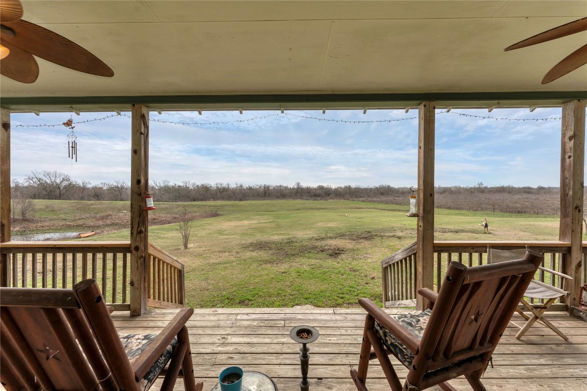Wooden deck with a ceiling fan, a rural view, and a lawn