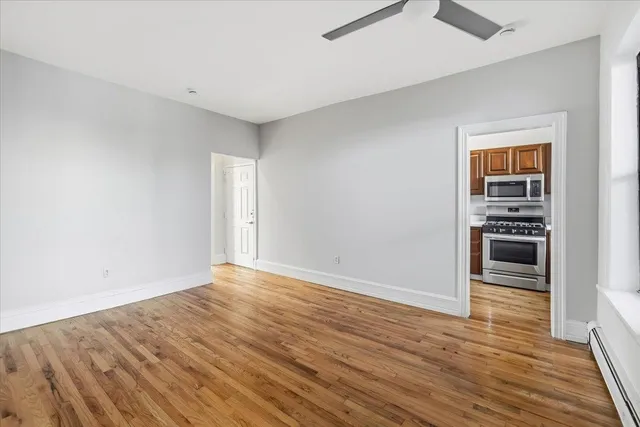 a view of empty room with wooden floor and kitchen view