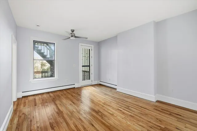 an empty room with wooden floor chandelier fan and windows