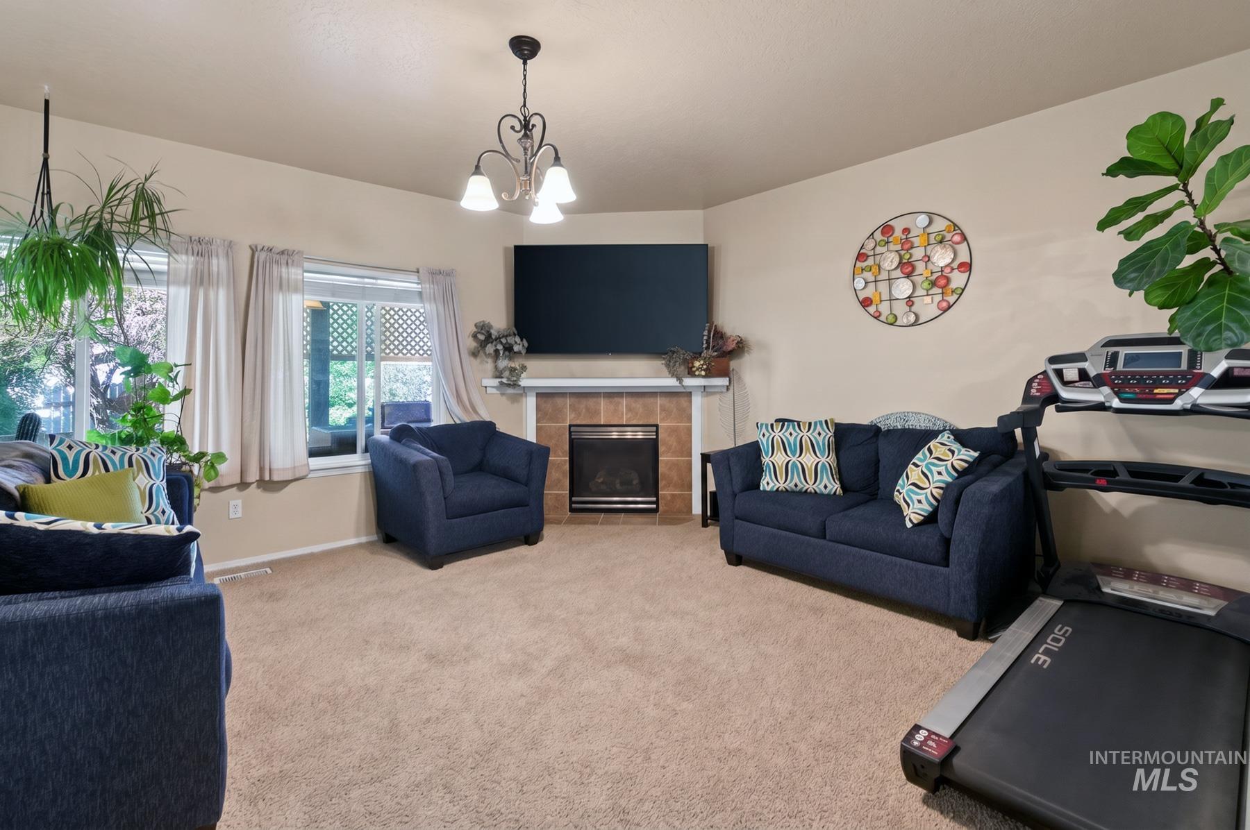 5020 Northrup Way Caldwell, ID 83607 - Photo 9 of 36 Inviting living area featuring a corner fireplace with a tile surround and mantel, carpeted flooring, multiple windows, and a decorative chandelier