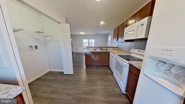 a kitchen with stainless steel appliances granite countertop a refrigerator a sink dishwasher a stove and white countertops with wooden floor
