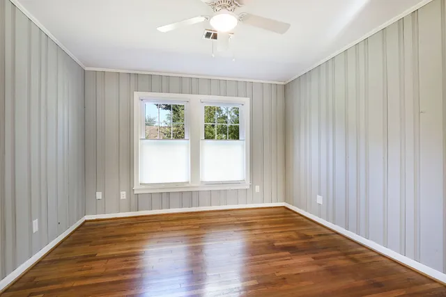 an empty room with wooden floor chandelier fan and windows