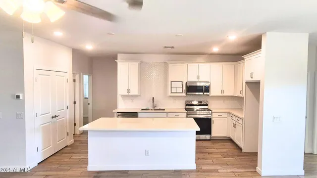 a kitchen with stainless steel appliances a stove a sink dishwasher a refrigerator and white cabinets with wooden floor