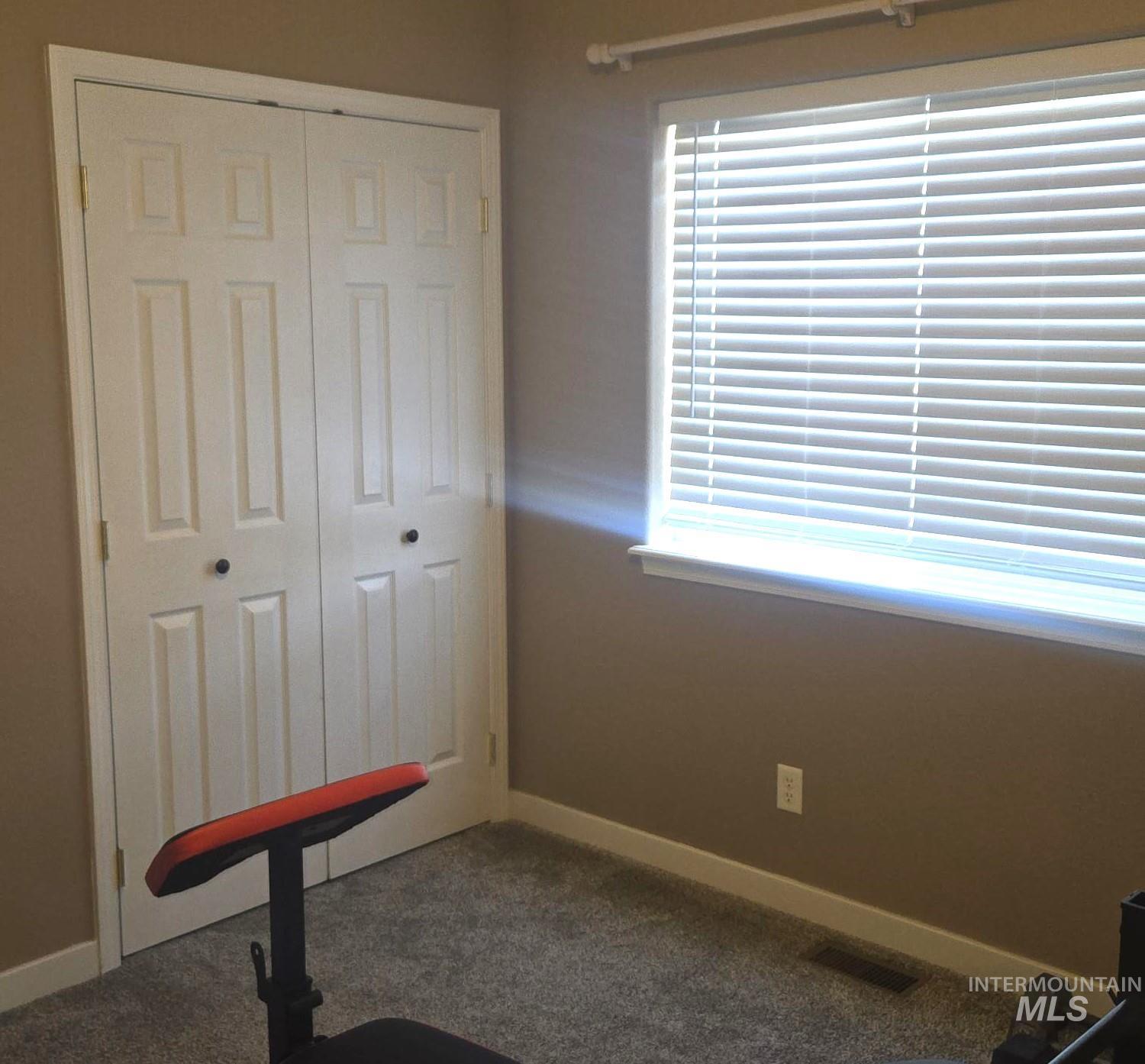 2480 West 9th Street Weiser, ID 83672 - Photo 11 of 17 Room featuring a wide window with blinds, bi-fold closet doors, neutral wall paint, white trim, and carpeted flooring