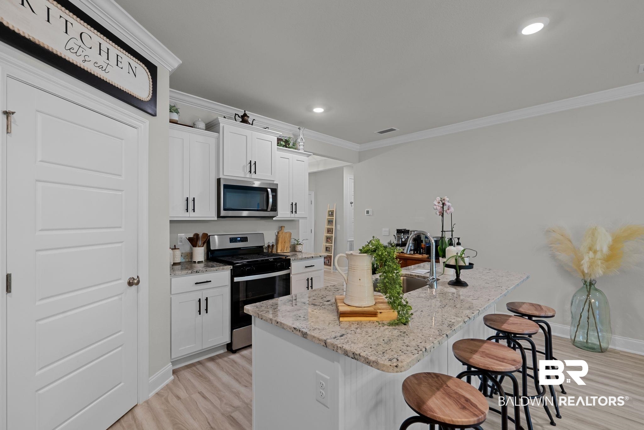 13966 Antler Hl Road Daphne, AL 36527 - Photo 8 of 44 Contemporary kitchen featuring an island with stone countertops and seating, white cabinetry with dark hardware, stainless steel appliances, and wood-finish flooring