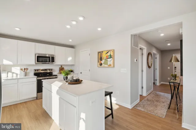 a kitchen with stainless steel appliances kitchen island granite countertop a stove top oven a sink a refrigerator and white cabinets with wooden floor