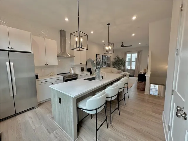 a kitchen with stainless steel appliances granite countertop a kitchen island a stove a refrigerator a sink a dining table and chairs with wooden floor