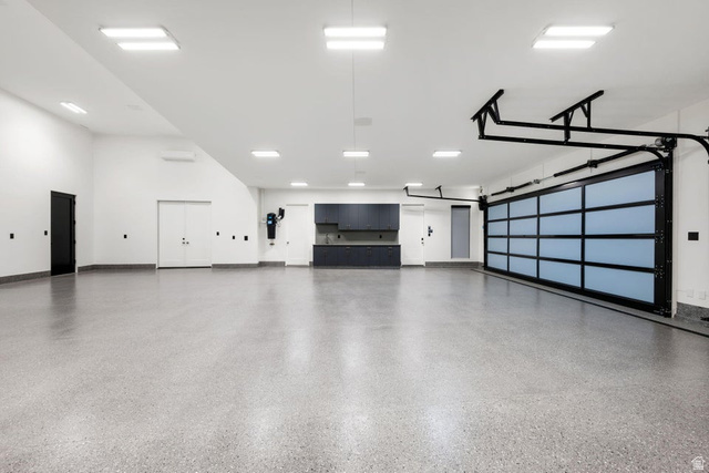 2867 East Granite Way St. George, UT 84790 - Photo 59 of 69 Spacious garage featuring a glass-paneled sectional door, light gray epoxy flooring, built-in dark cabinetry with a countertop, recessed square lighting, and white walls