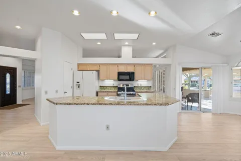 a large kitchen with granite countertop a sink dishwasher a stove and white cabinets with wooden floor