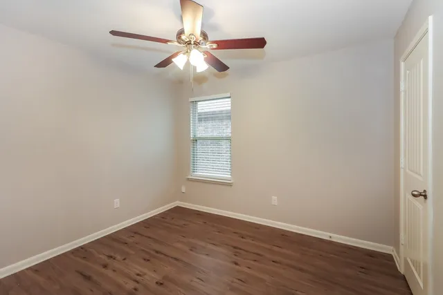 an empty room with wooden floor fan and windows