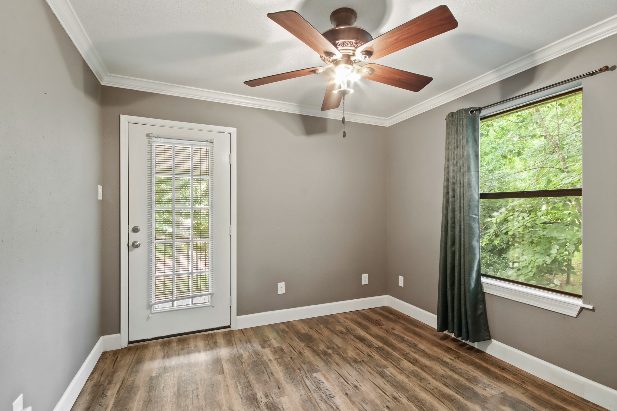 35 Susan Drive Cleveland, TX 77327 - Photo 22 of 33 This room features laminate wood flooring, neutral gray walls, and a ceiling fan with light. It has a large window with a view of greenery and a door with glass panels, providing ample natural light.