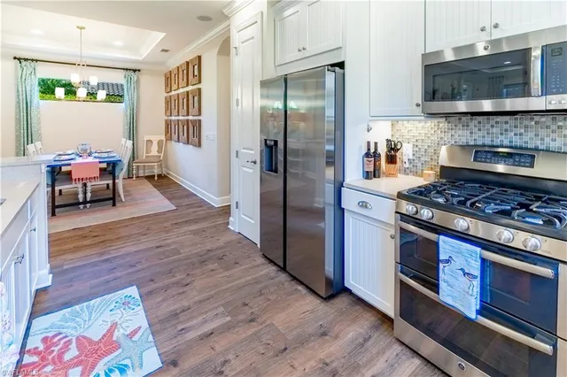 a kitchen with stainless steel appliances granite countertop a refrigerator a sink a stove and white cabinets with wooden floor